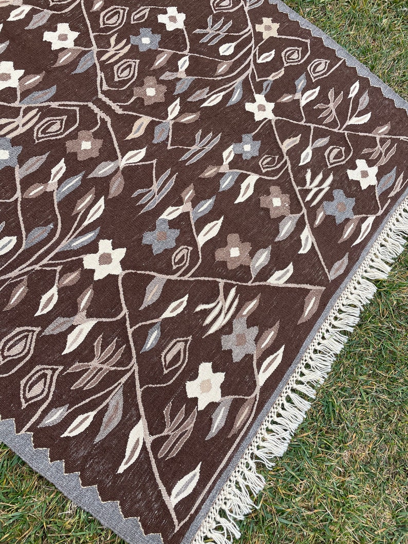 Puede incluir: Una alfombra de color marr&oacute;n y crema con un borde de flecos. La alfombra presenta un dise&ntilde;o floral con hojas y flores.