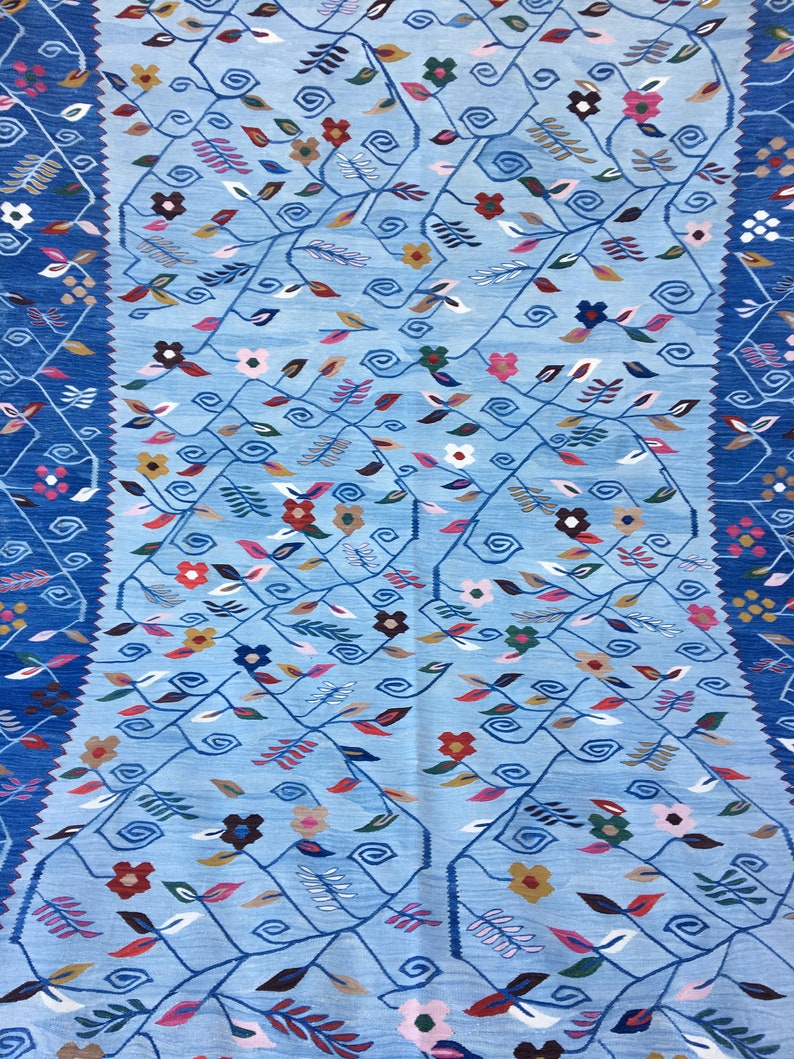 May include: A light blue rug with a floral pattern. The design features winding vines with leaves and flowers in shades of red, pink, yellow, and brown. The border is a darker blue with geometric patterns.