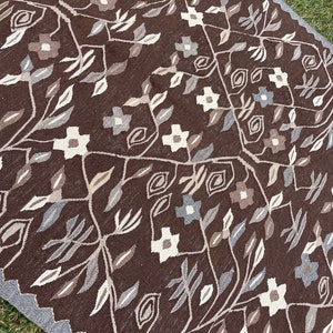 Puede incluir: Una alfombra marr&oacute;n con un patr&oacute;n floral en tonos de blanco, gris y marr&oacute;n. La alfombra tiene un dise&ntilde;o geom&eacute;trico con motivos repetidos de hojas y flores.