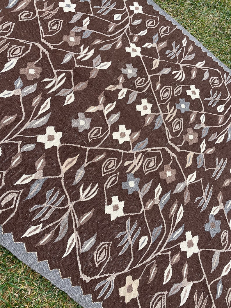 Puede incluir: Una alfombra marr&oacute;n con un patr&oacute;n floral en tonos de blanco, gris y marr&oacute;n. La alfombra tiene un dise&ntilde;o geom&eacute;trico con motivos repetidos de hojas y flores.