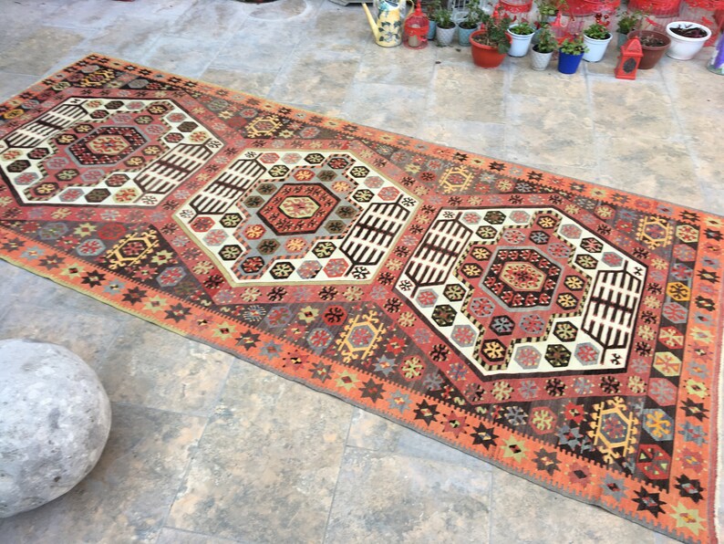 May include: A traditional Turkish rug with a geometric pattern in shades of red, orange, brown, and white. The rug has a central medallion with a hexagonal design and a border with a repeating star pattern.