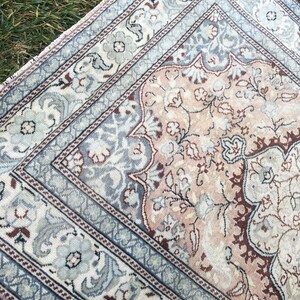 Peut inclure: Un tapis vintage avec un motif floral dans des tons de rose, bleu et marron. Le tapis a une bordure avec un motif r&eacute;p&eacute;titif.