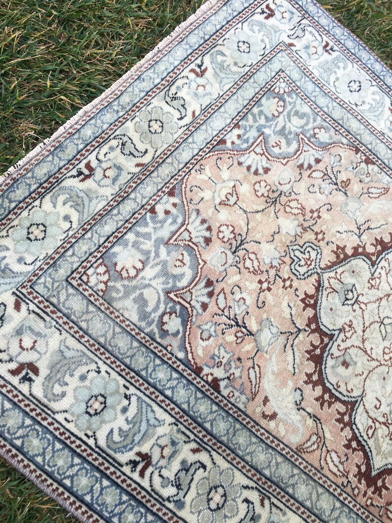 Peut inclure: Un tapis vintage avec un motif floral dans des tons de rose, bleu et marron. Le tapis a une bordure avec un motif r&eacute;p&eacute;titif.