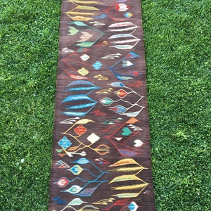 Puede incluir: Una alfombra larga y estrecha con fondo marr&oacute;n y un patr&oacute;n geom&eacute;trico colorido. El patr&oacute;n presenta una variedad de formas, incluyendo diamantes, hojas y espirales. La alfombra est&aacute; tejida con una variedad de colores, incluyendo rojo, azul, verde, amarillo y blanco.
