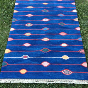Puede incluir: Una alfombra azul con un patr&oacute;n geom&eacute;trico de &oacute;valos rojos, rosas, amarillos y verdes. La alfombra tiene un borde de flecos blancos.