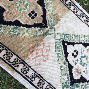 May include: A vintage rug with a geometric pattern in shades of green, black, and pink. The rug has a white background and a black border.