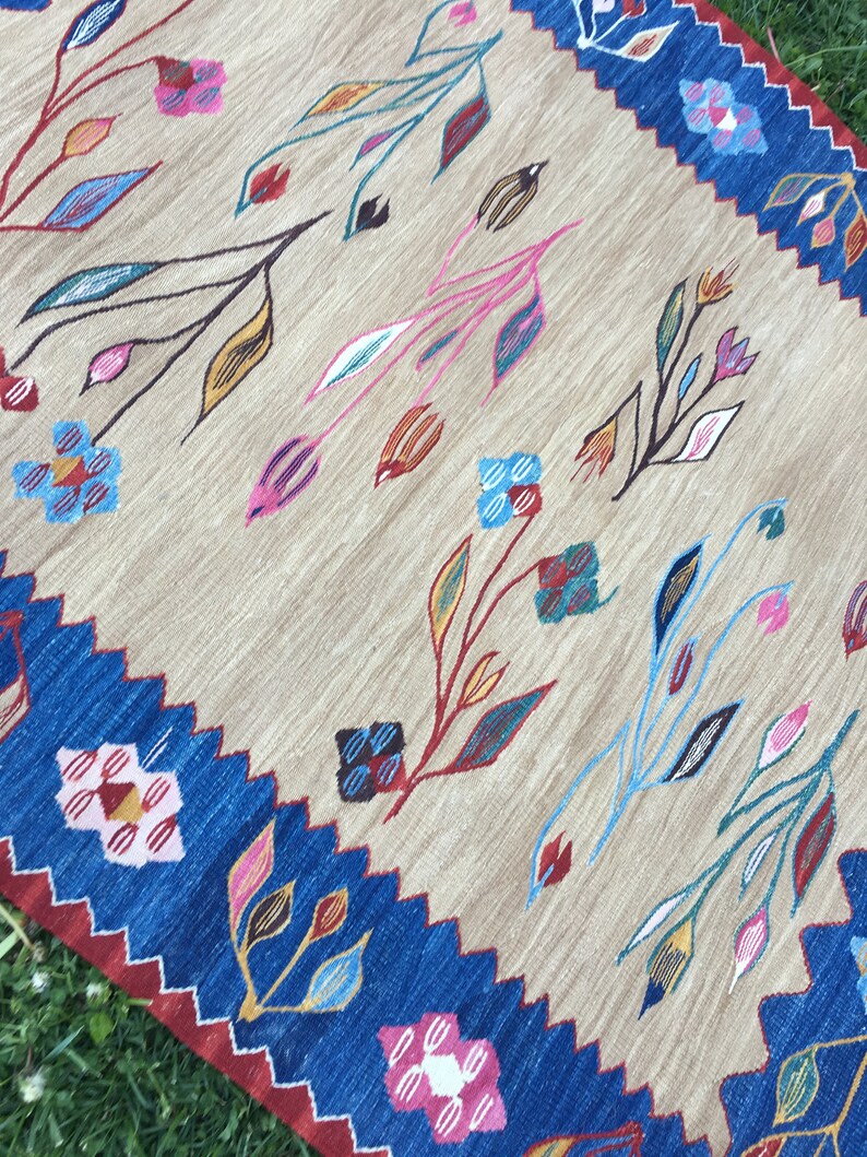 May include: A beige rug with a blue border and a floral pattern in shades of pink, blue, yellow, and green.