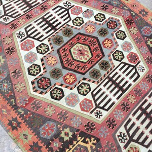May include: A colorful rug with a geometric pattern in shades of red, blue, green, and brown. The rug has a traditional design with intricate details.