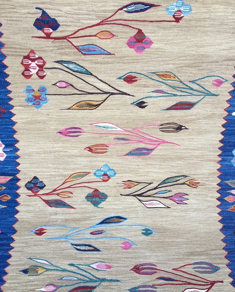 May include: A beige rug with a woven design of colorful flowers and leaves. The rug has a blue border.