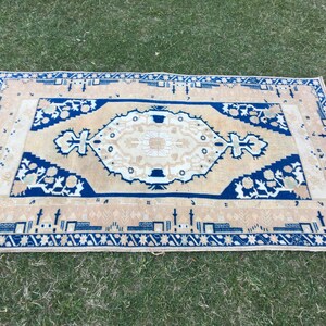 May include: A beige rug with a blue and white geometric pattern. The rug has a fringe border.
