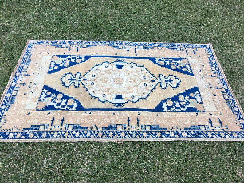 May include: A beige rug with a blue and white geometric pattern. The rug has a fringe border.