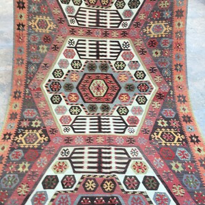 May include: A traditional Turkish rug with a geometric pattern in shades of red, blue, green, and white. The rug features a central medallion with intricate details and a repeating border.
