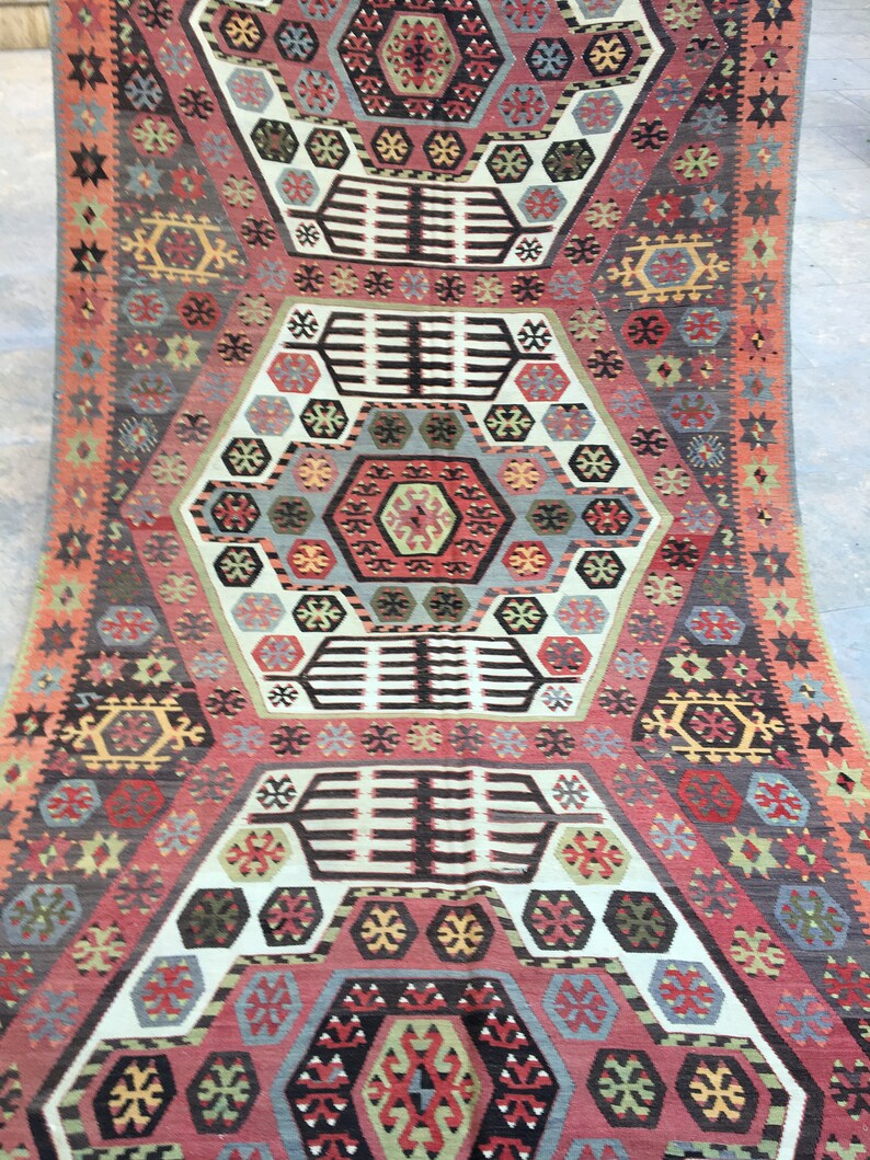 May include: A traditional Turkish rug with a geometric pattern in shades of red, blue, green, and white. The rug features a central medallion with intricate details and a repeating border.