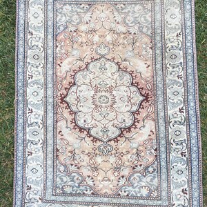 Peut inclure: Un tapis vintage avec un motif floral rose p&acirc;le et brun. Le tapis a une bordure bleu clair avec un motif floral.