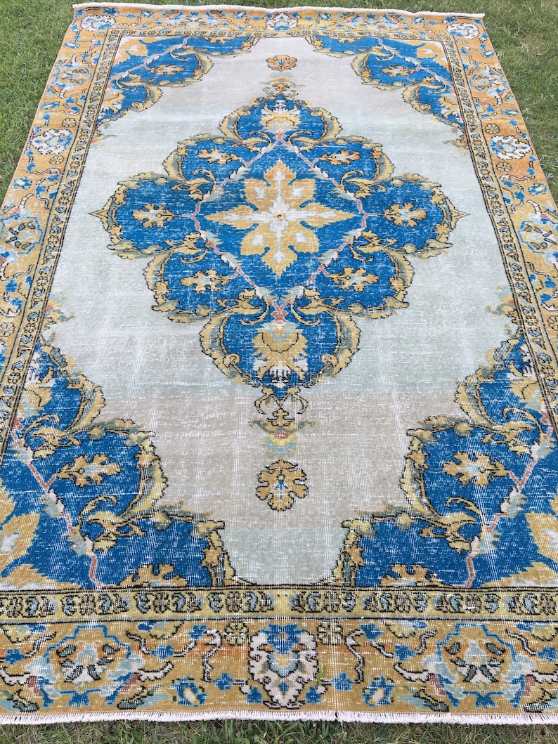 May include: A large, rectangular rug with an ornate, traditional design. The rug features a central medallion and corner elements in shades of blue, gold, and cream. The border is a mix of gold and blue, with a cream-colored fringe.
