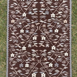 Puede incluir: Una alfombra de color marr&oacute;n y blanco con un dise&ntilde;o geom&eacute;trico. La alfombra tiene un borde de flecos.