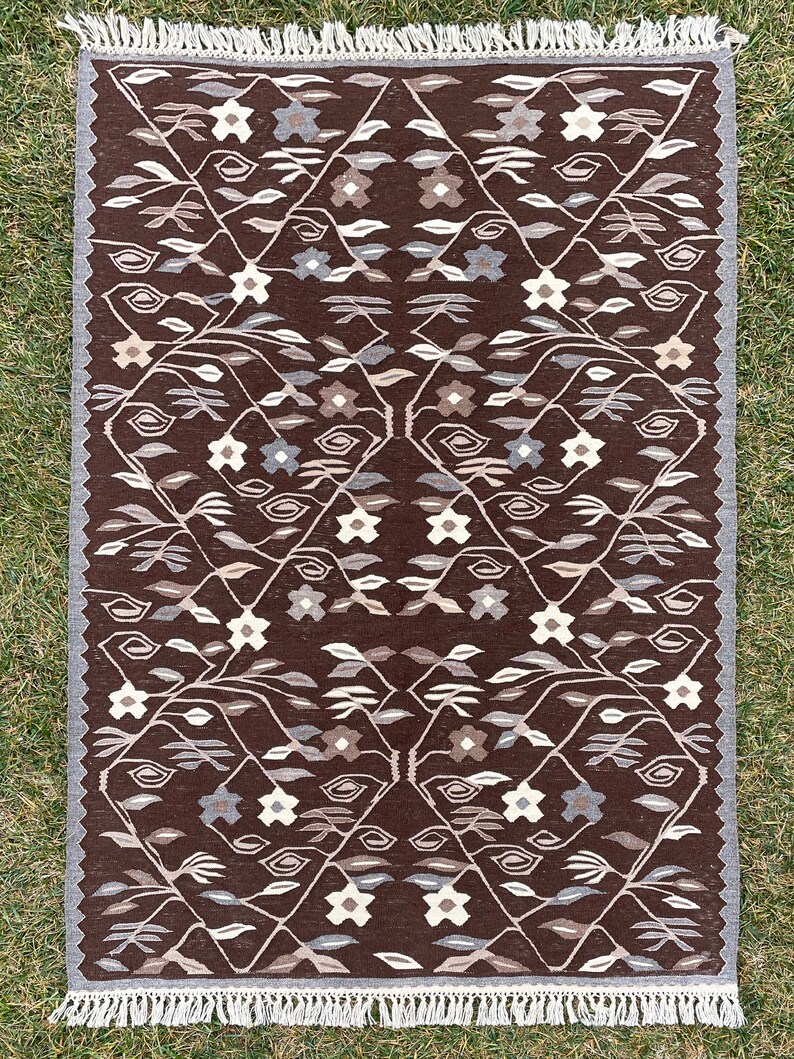 Puede incluir: Una alfombra de color marr&oacute;n y blanco con un dise&ntilde;o geom&eacute;trico. La alfombra tiene un borde de flecos.