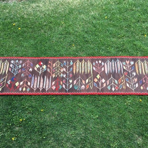 Puede incluir: Una alfombra larga y estrecha con fondo marr&oacute;n y un estampado floral colorido. La alfombra tiene un borde rojo y flecos en los extremos.