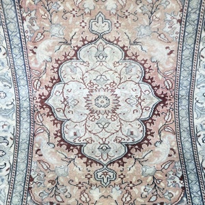 Peut inclure: Un tapis vintage avec un motif floral dans des tons de rose, bleu et blanc. Le tapis a un m&eacute;daillon central avec un motif r&eacute;p&eacute;titif de fleurs et de feuilles.