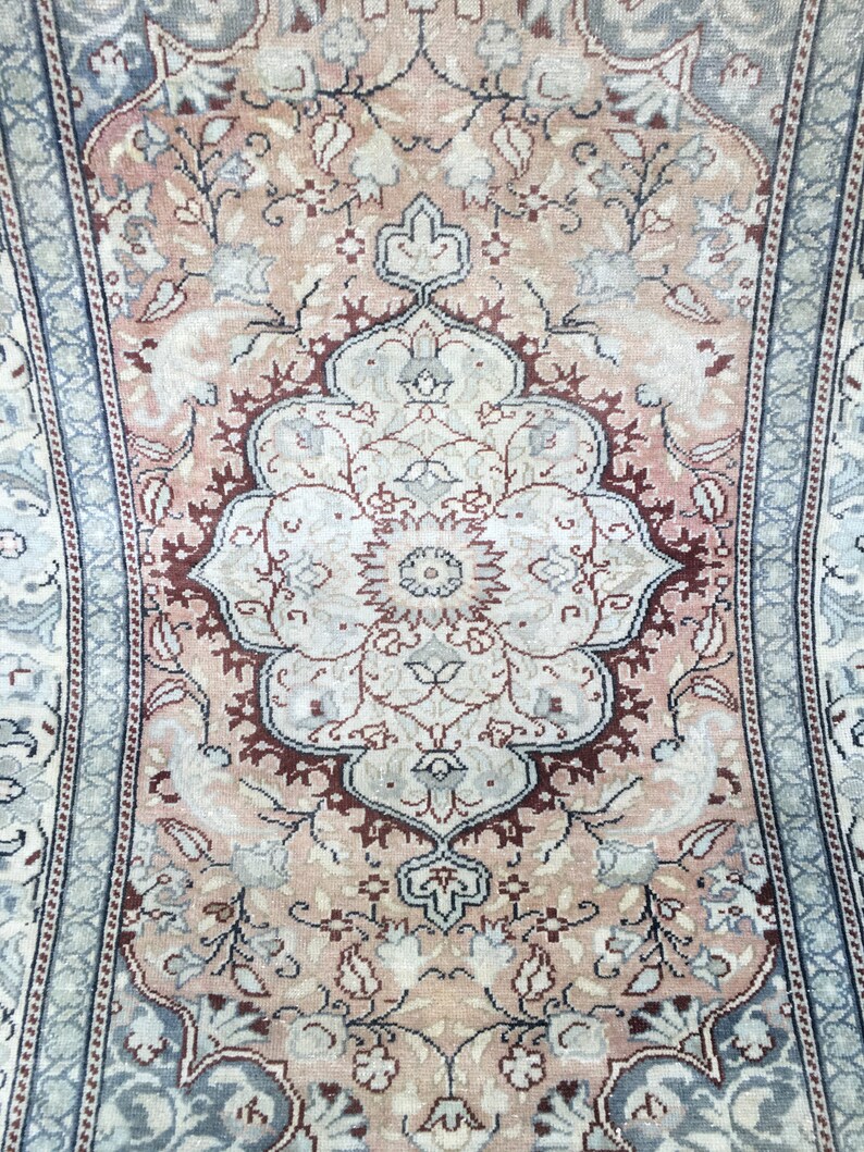 Peut inclure: Un tapis vintage avec un motif floral dans des tons de rose, bleu et blanc. Le tapis a un m&eacute;daillon central avec un motif r&eacute;p&eacute;titif de fleurs et de feuilles.