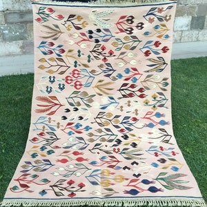 Puede incluir: Una alfombra rosa y crema con un patr&oacute;n floral. La alfombra presenta una variedad de colores, incluyendo rojo, azul, verde y amarillo. La alfombra tiene un borde de flecos.