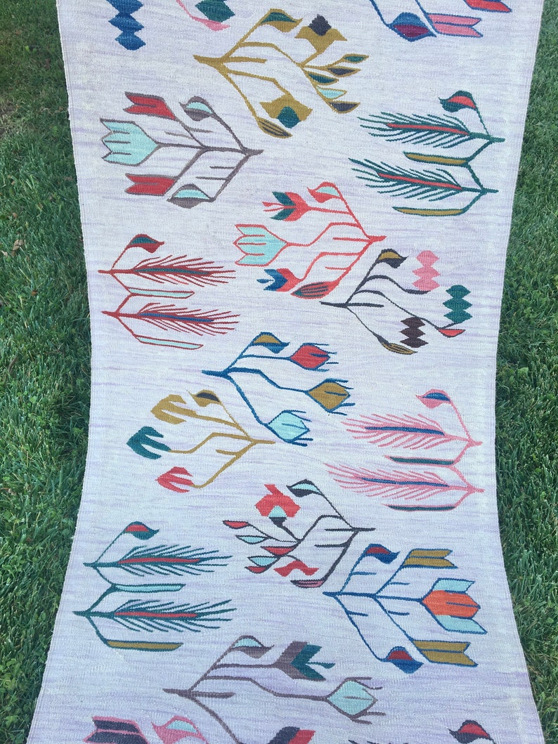 May include: A white rug with a repeating pattern of stylized floral designs in shades of red, blue, green, and pink.