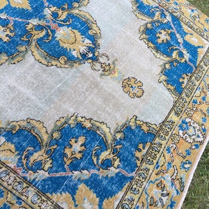 May include: A vintage rug with a distressed appearance. The rug features a central design in shades of blue and gold, with intricate floral patterns. The border is a darker blue and gold, with a cream-colored background.