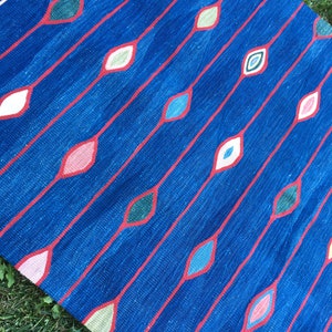 Puede incluir: Una alfombra azul con un patr&oacute;n repetitivo de l&iacute;neas rojas y formas de diamantes de colores. La alfombra est&aacute; hecha de tejido tejido y tiene una superficie texturizada.