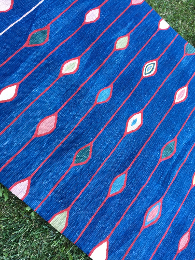Puede incluir: Una alfombra azul con un patr&oacute;n repetitivo de l&iacute;neas rojas y formas de diamantes de colores. La alfombra est&aacute; hecha de tejido tejido y tiene una superficie texturizada.