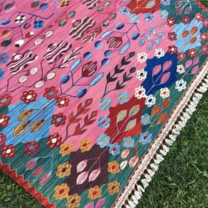 May include: A colourful rug with a floral pattern in shades of pink, blue, green, and red. The rug has a fringed border.