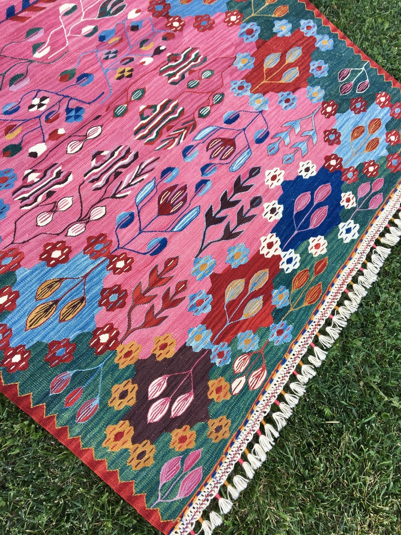 May include: A colourful rug with a floral pattern in shades of pink, blue, green, and red. The rug has a fringed border.