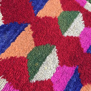 Puede incluir: Una alfombra geom&eacute;trica colorida con un dise&ntilde;o de patchwork. La alfombra est&aacute; hecha de hilo grueso y esponjoso en tonos de rojo, azul, verde, rosa, blanco y naranja.