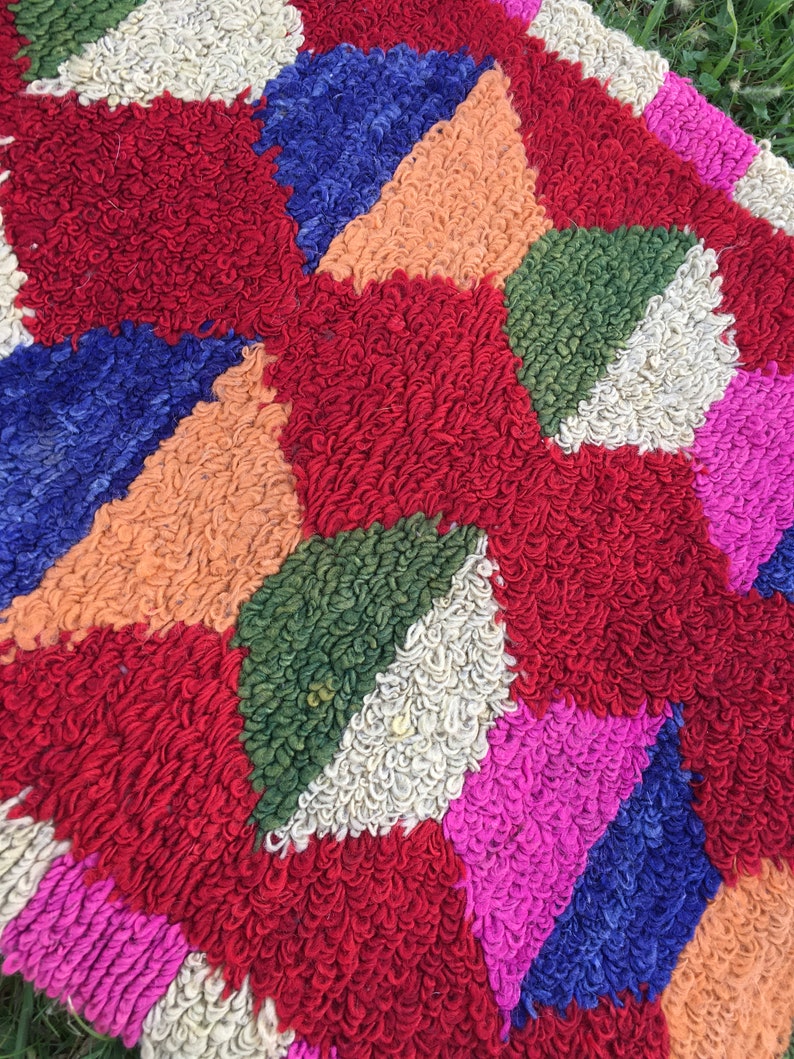 Puede incluir: Una alfombra geom&eacute;trica colorida con un dise&ntilde;o de patchwork. La alfombra est&aacute; hecha de hilo grueso y esponjoso en tonos de rojo, azul, verde, rosa, blanco y naranja.