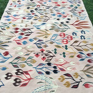 Puede incluir: Una alfombra rosa con un estampado floral colorido. La alfombra tiene un borde de flecos y est&aacute; hecha de tejido tejido.