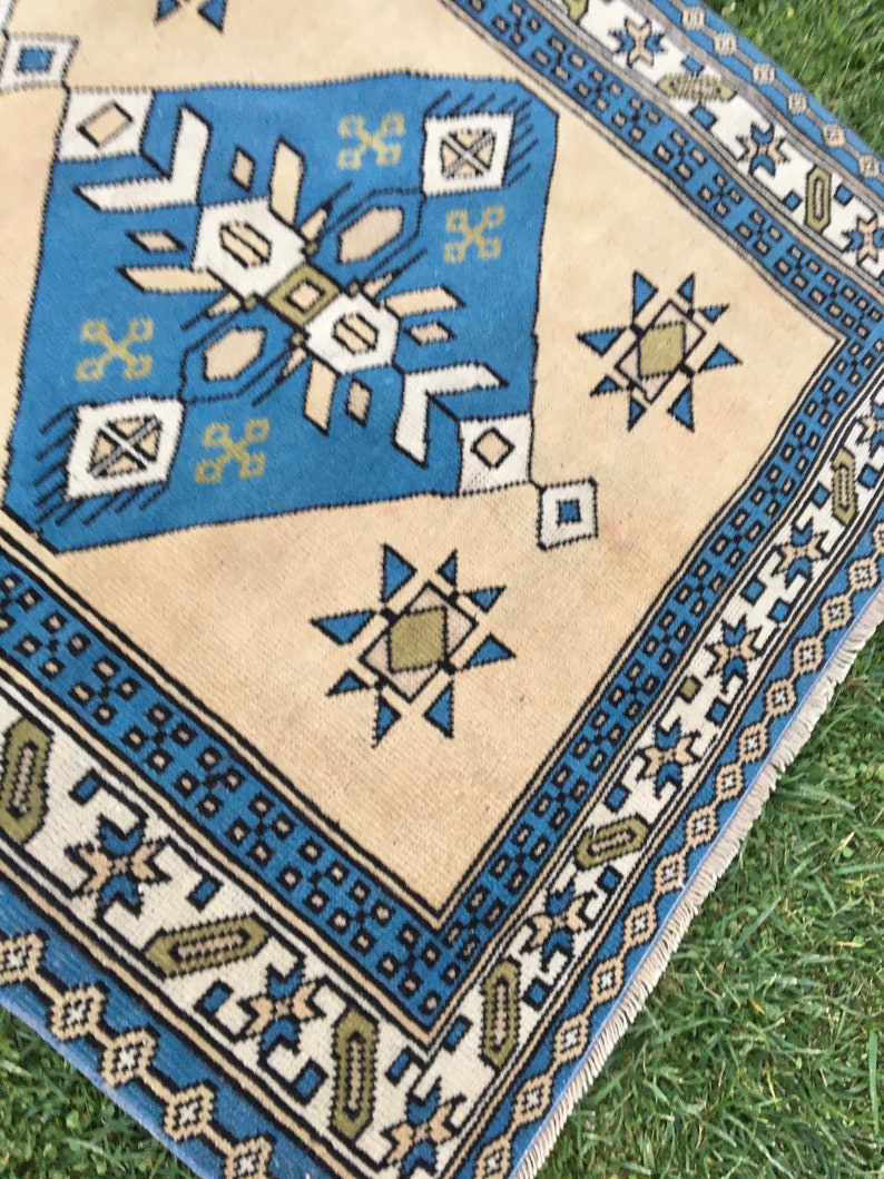 May include: A blue and beige patterned rug with a geometric design. The rug has a fringe border.
