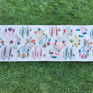 May include: A long, rectangular rug with a white background and a repeating pattern of stylized flowers and leaves in shades of pink, blue, green, yellow, and red.
