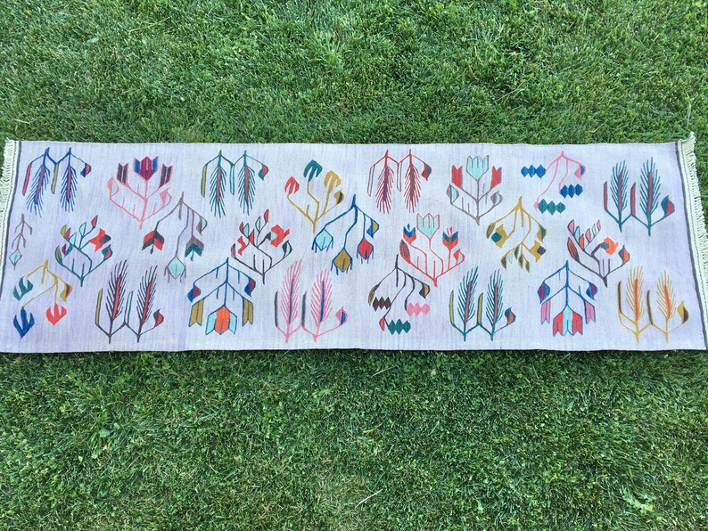 May include: A long, rectangular rug with a white background and a repeating pattern of stylized flowers and leaves in shades of pink, blue, green, yellow, and red.