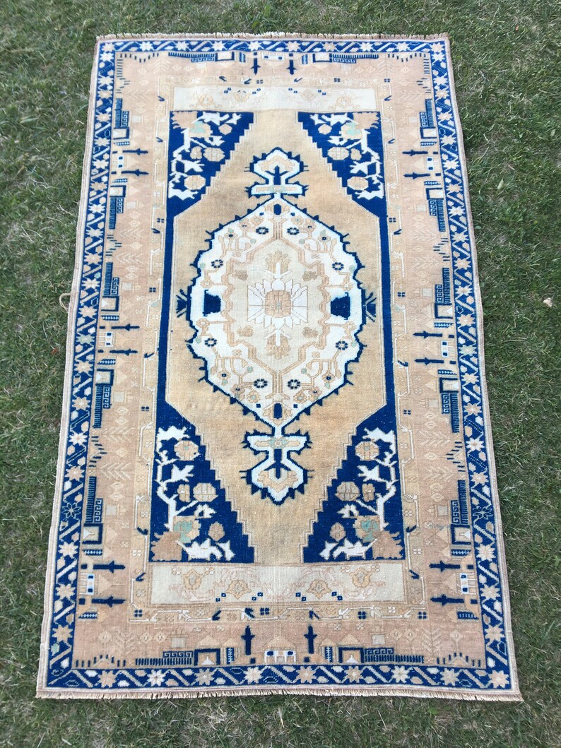 May include: A vintage rug with a beige background and a blue and white geometric pattern. The rug has a fringe border.