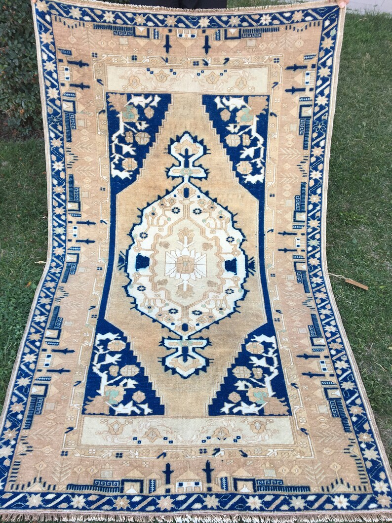 May include: A vintage rug with a beige background and a blue border. The rug has a traditional Persian design with intricate floral patterns and geometric shapes.