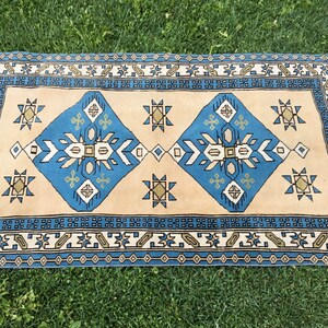 May include: A blue and beige patterned rug with a geometric design. The rug has a border with a repeating pattern of small squares and diamonds.
