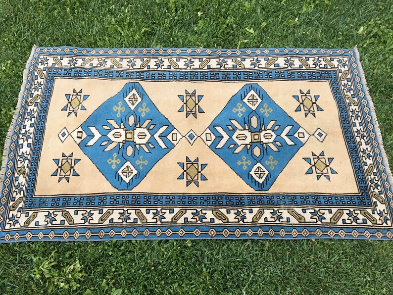 May include: A blue and beige patterned rug with a geometric design. The rug has a border with a repeating pattern of small squares and diamonds.