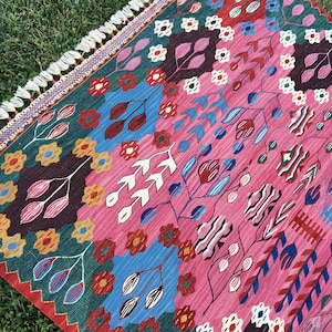 May include: A colourful rug with a geometric pattern featuring pink, blue, green, red and white. The rug has a fringed border.