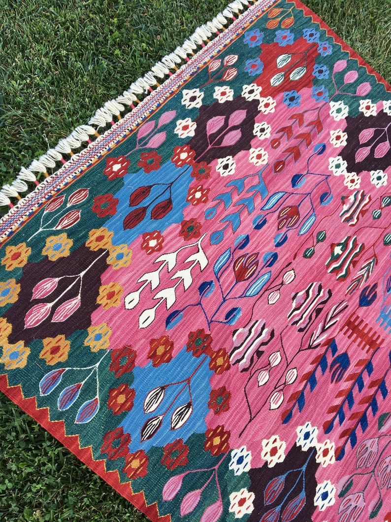 May include: A colourful rug with a geometric pattern featuring pink, blue, green, red and white. The rug has a fringed border.