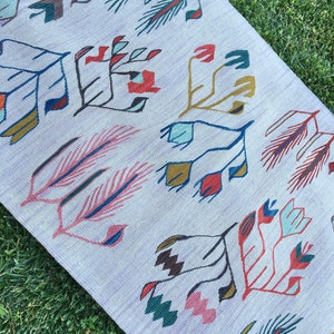 May include: A white rug with a geometric pattern of stylized flowers and leaves in shades of red, blue, green, and brown.