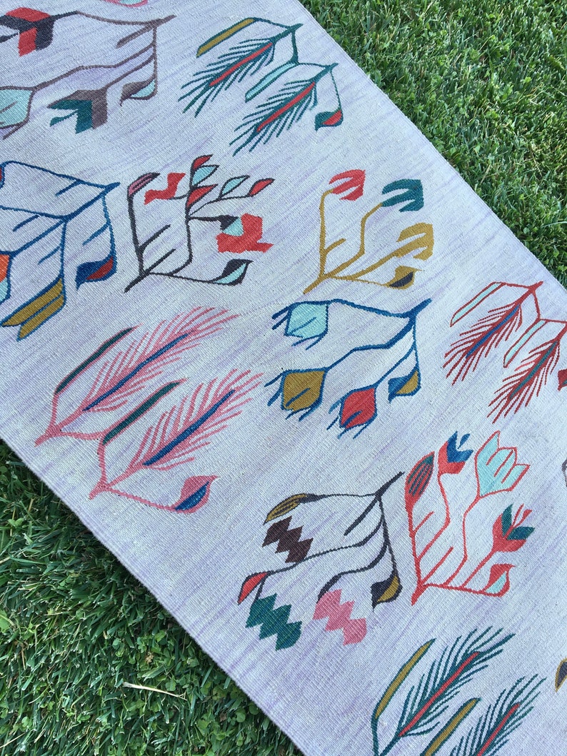 May include: A white rug with a geometric pattern of stylized flowers and leaves in shades of red, blue, green, and brown.