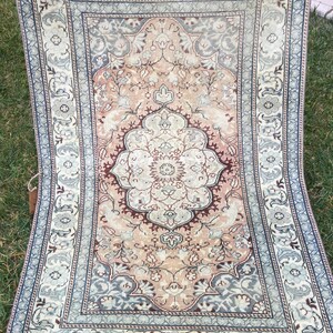 Peut inclure: Un tapis vintage avec un motif floral dans des tons de rose, bleu et marron. Le tapis a un m&eacute;daillon central et une bordure aux motifs complexes.