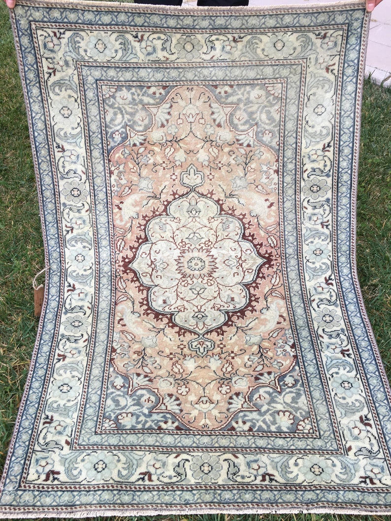 Peut inclure: Un tapis vintage avec un motif floral dans des tons de rose, bleu et marron. Le tapis a un m&eacute;daillon central et une bordure aux motifs complexes.