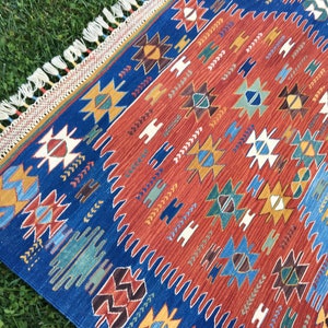 Puede incluir: Una alfombra colorida con un patr&oacute;n geom&eacute;trico en tonos de azul, rojo, amarillo y verde. La alfombra tiene un borde de flecos y est&aacute; hecha de tejido tejido.