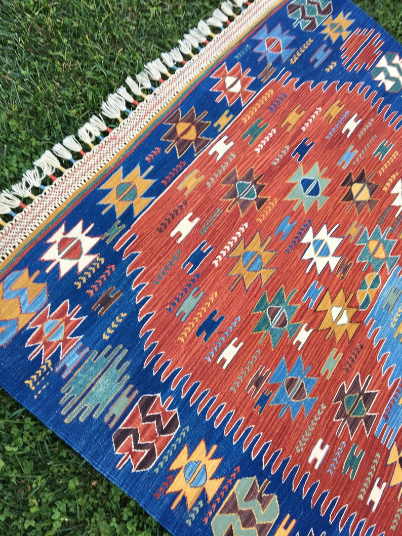 Puede incluir: Una alfombra colorida con un patr&oacute;n geom&eacute;trico en tonos de azul, rojo, amarillo y verde. La alfombra tiene un borde de flecos y est&aacute; hecha de tejido tejido.