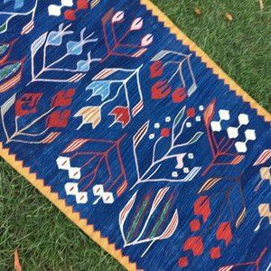 May include: A blue and yellow patterned rug with a floral design. The rug has a geometric pattern with red, white, and blue flowers.